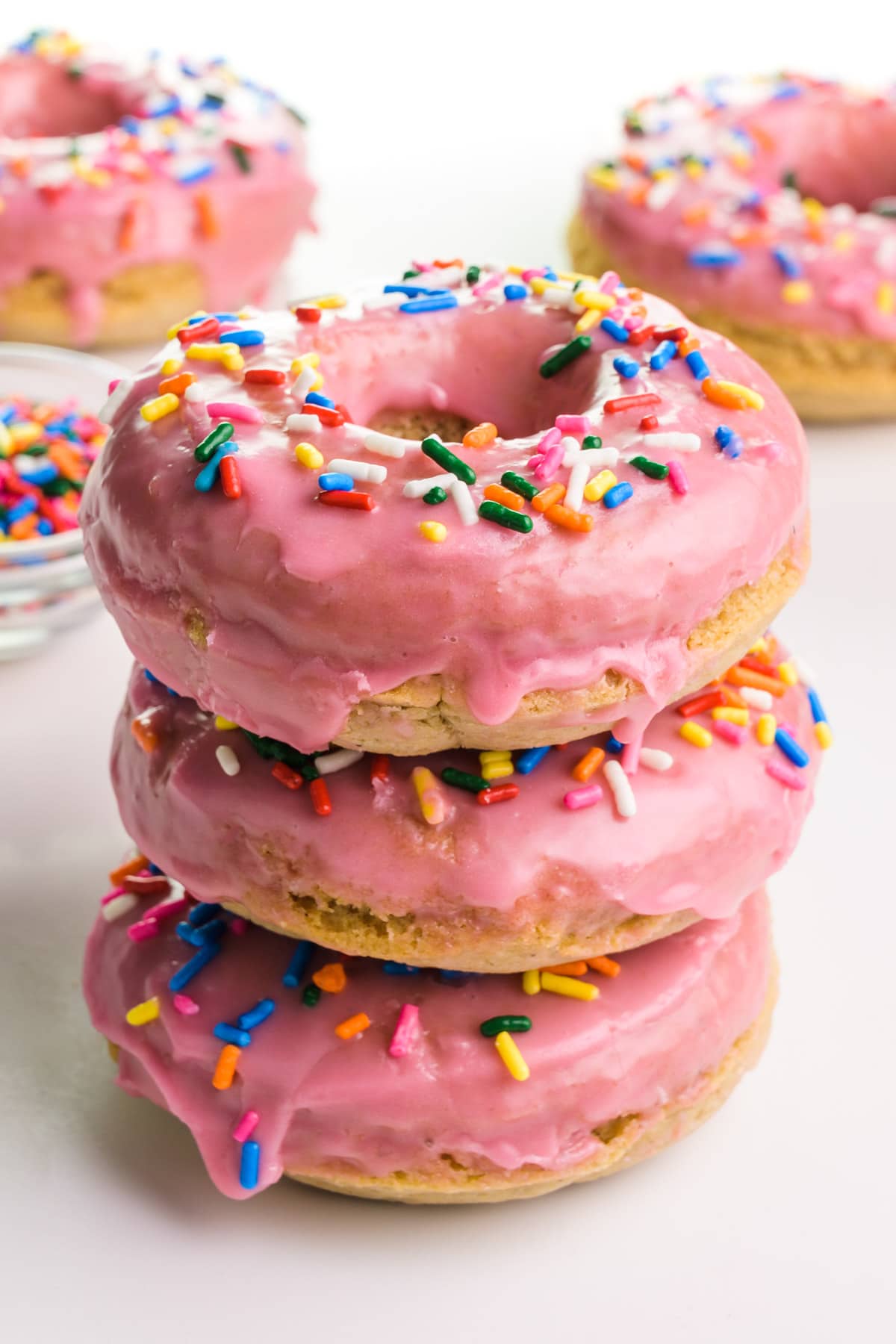 Three vegan gluten-free donuts are stacked and sit in front of more donuts in the background.
