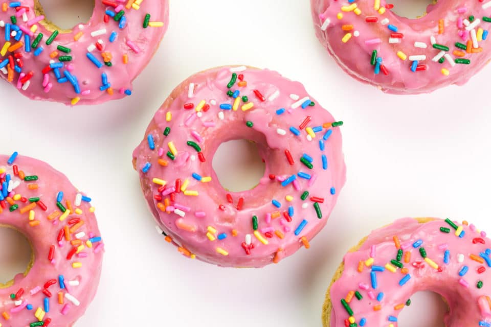Looking down on pink donuts with sprinkles on a white counter top.