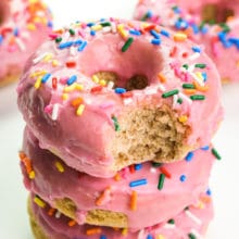 A stack of vegan gluten-free donuts shows the top one with a bite taken out.