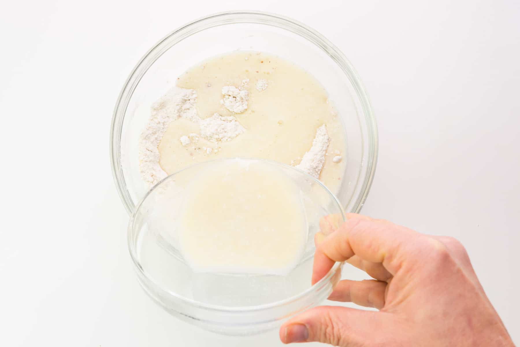 A hand holds a bowl, during wet ingredients into a bowl with flour ingredients.