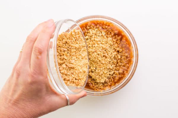 A hand holds a bowl of textured vegetable protein, pouring it into a bowl with a sauce mixture.