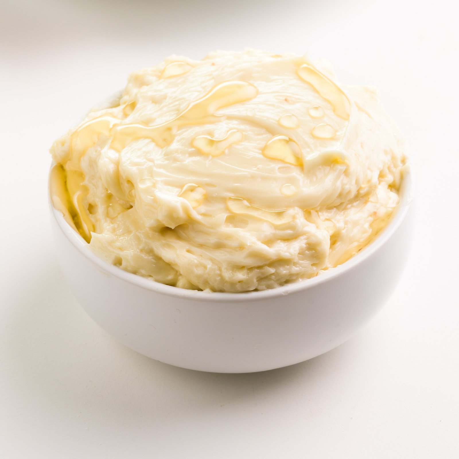 Honey butter is in a white bowl. There are drizzles of vegan honey on top.