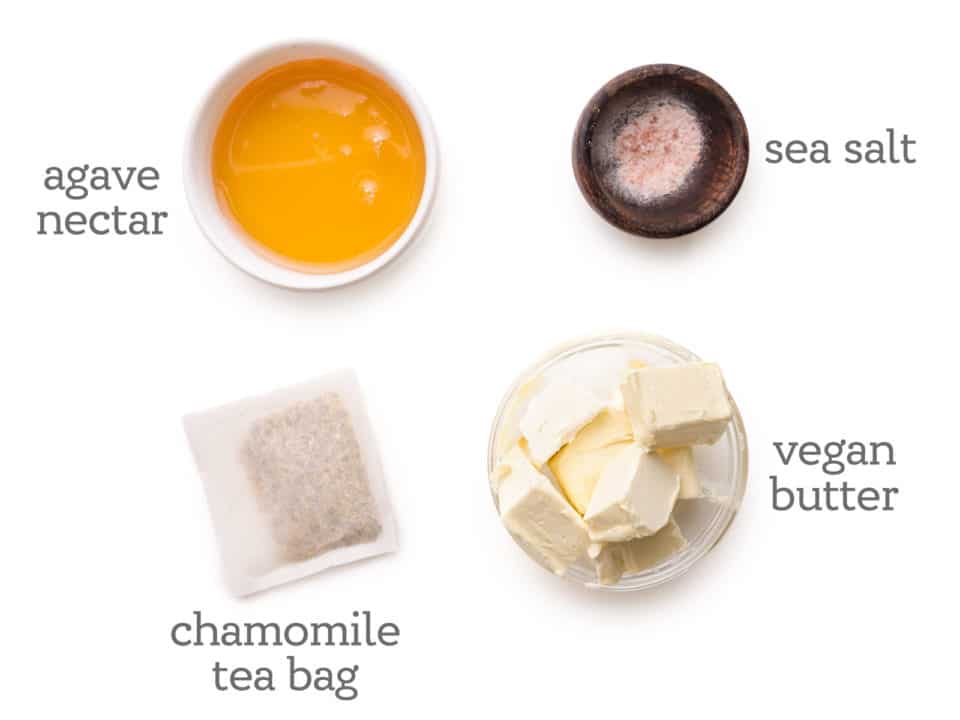 Ingredients are laid out on a white table. The labels next to them read, "agave nectar, sea salt, chamomile tea bag, and vegan butter."
