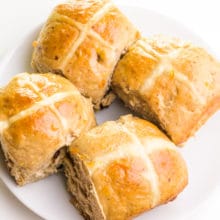 Looking down on a plate of several vegan hot cross buns on a plate.
