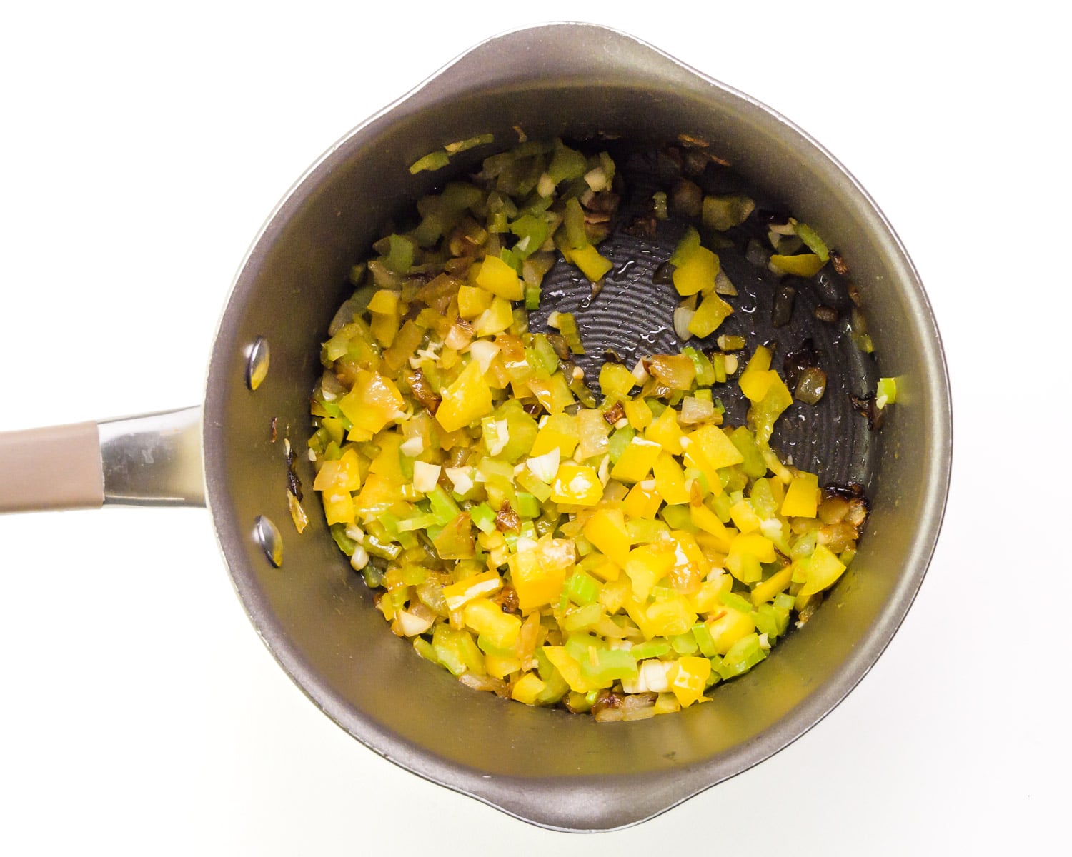 Cooked aromatic vegetables are in the bottom of a saucepan.