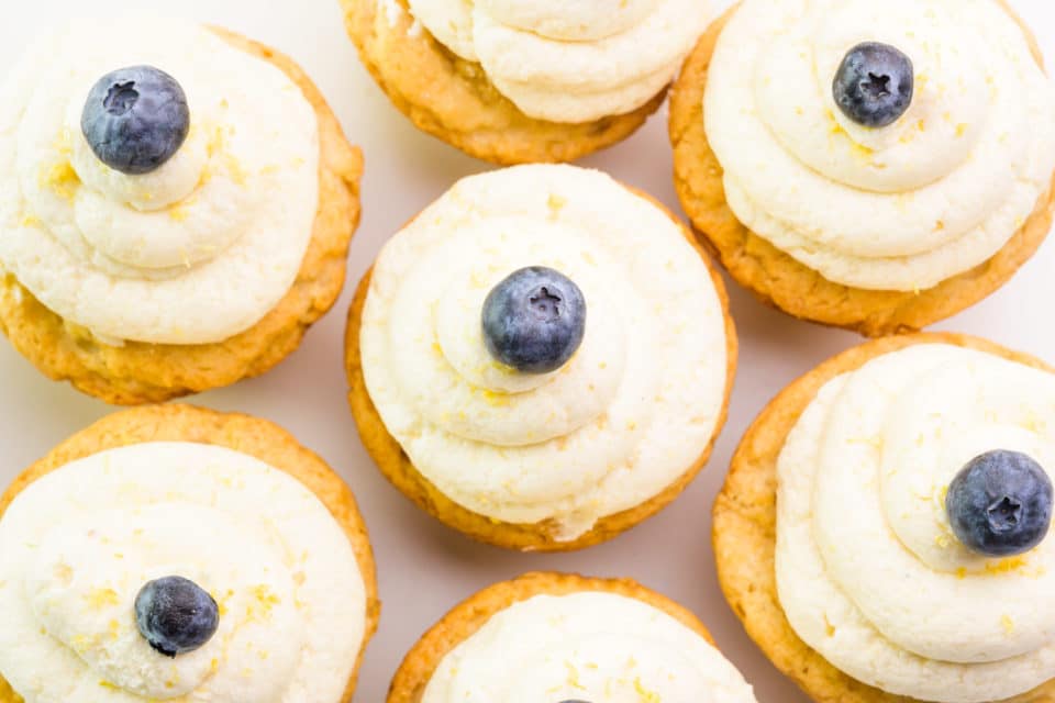Looking down on cupcakes with lemon frosting on them. Each one has a blueberry on top.