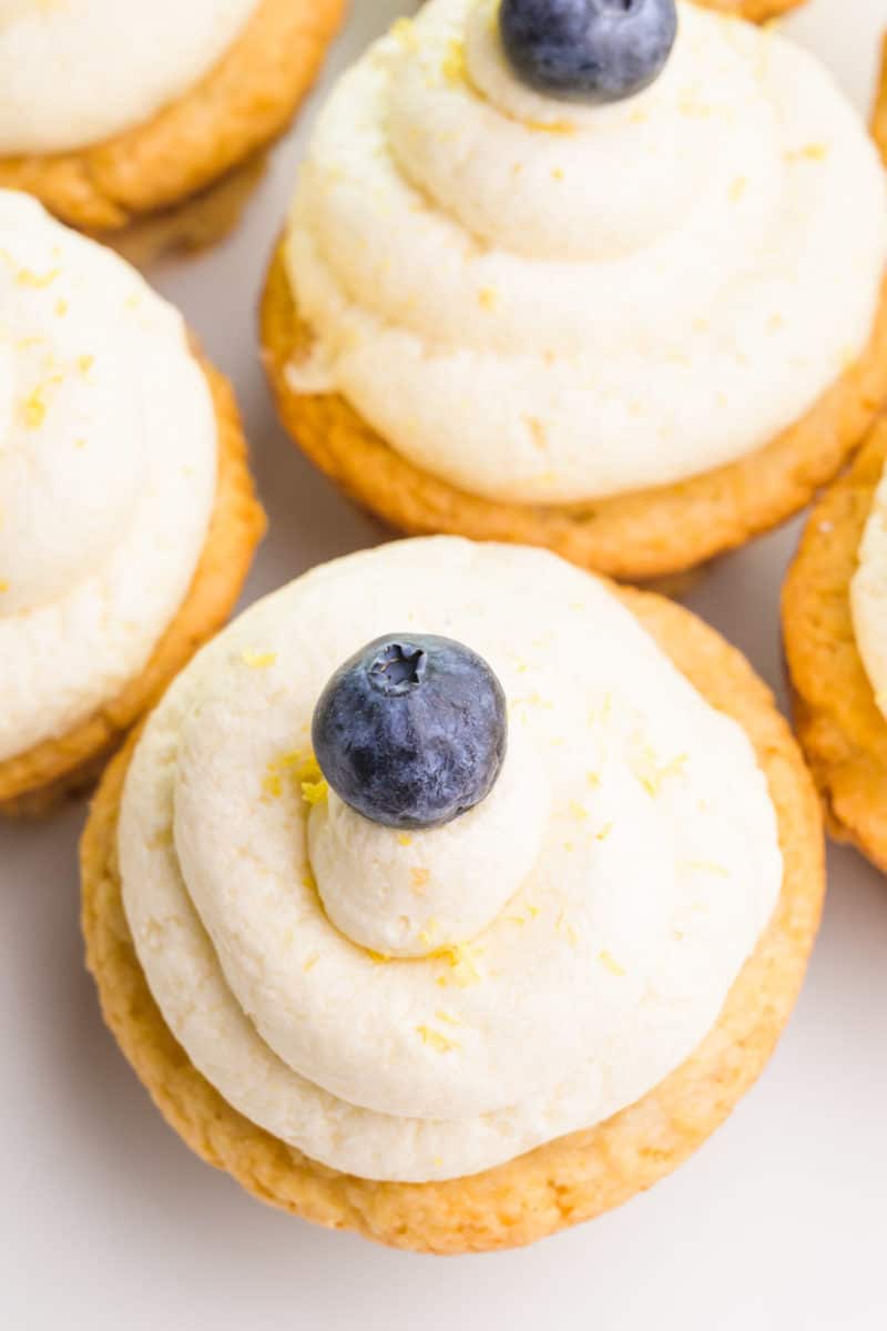 Looking down at the cupcakes with lemon frosting on them.  Each one has a blueberry on top.