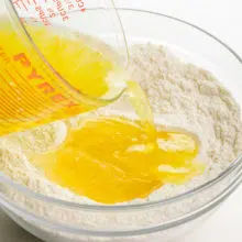 A lemon liquid mixture is being poured into a bowl with a flour mixture.