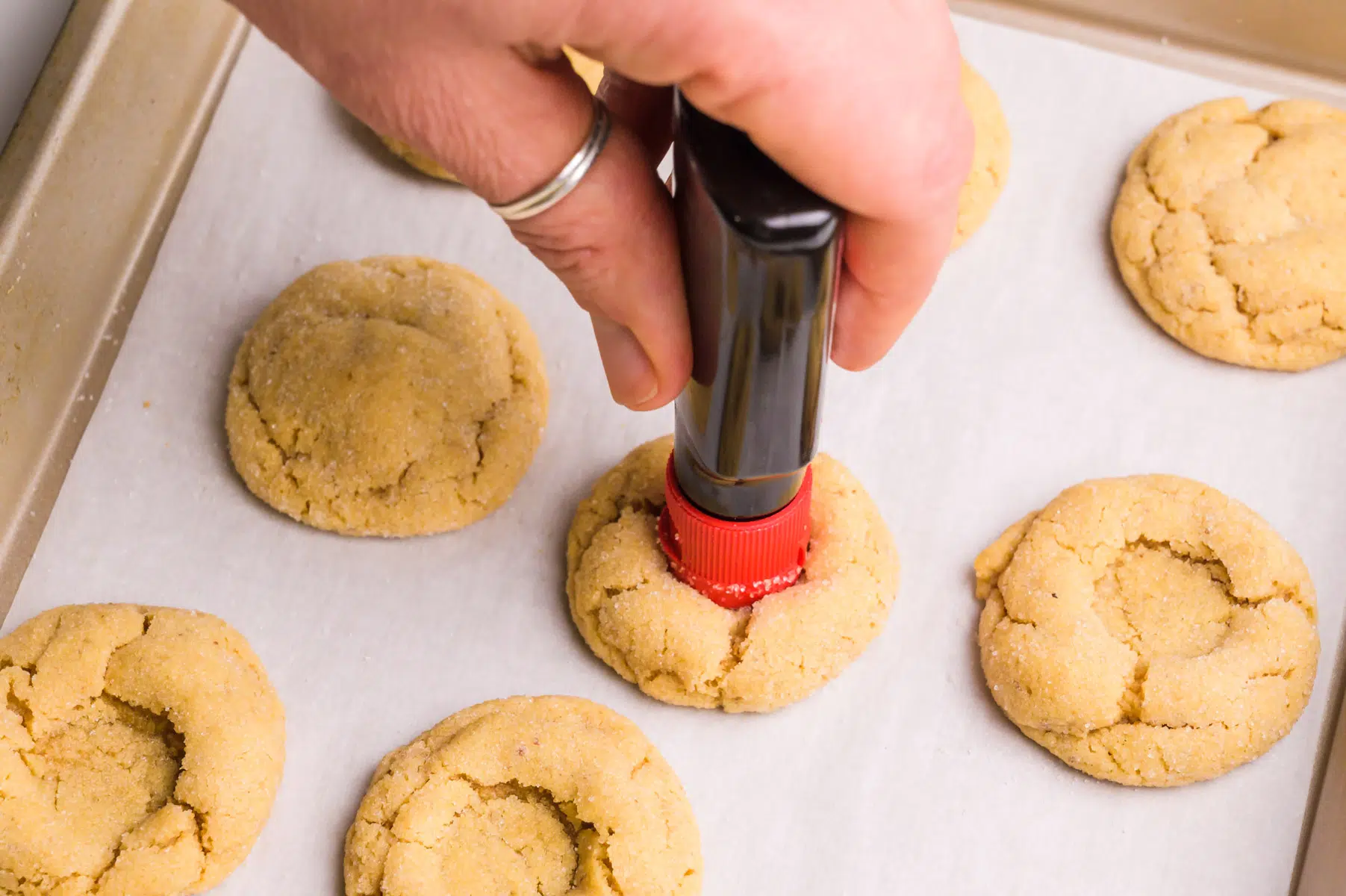 A hand holds an extract bottle, using the cap to make impressions in the center of peanut butter cookies.