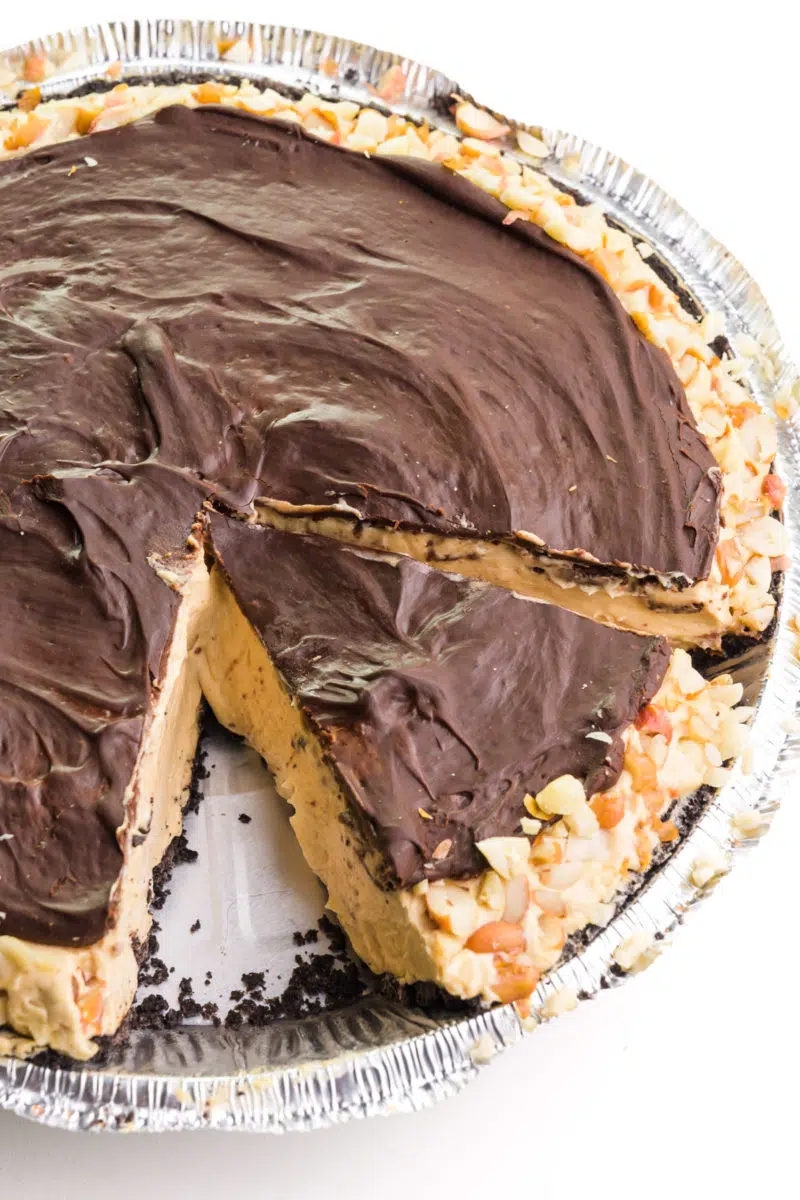 Looking down on a peanut butter pie with chocolate topping. Once slice is sitting separate from the rest of the pie in the pan.