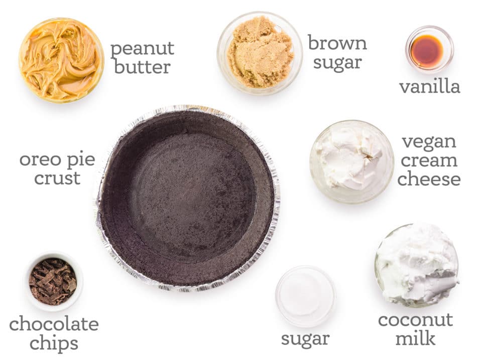 Ingredients are laid out on on a table. The labels next to them read, vanilla, vegan cream cheese, coconut milk, sugar, chocolate chips, peanut butter, and brown sugar. 