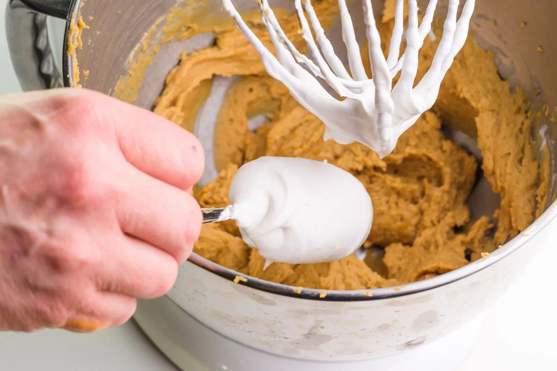 Whipped coconut topping is being added to a peanut butter mixture in a mixing bowl.