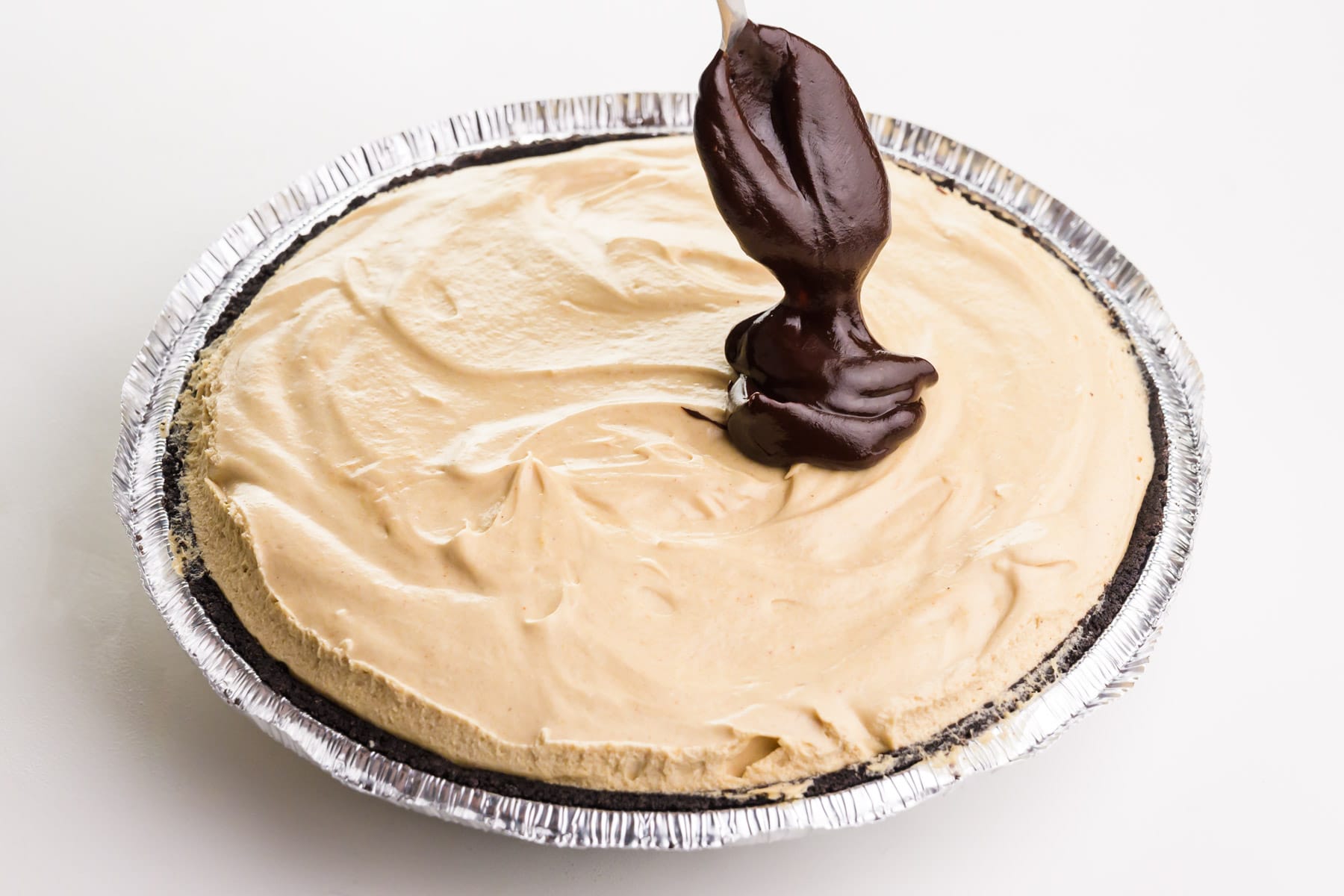 A spoonful of melted chocolate is being poured over a peanut butter pie.