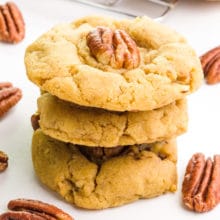 A stack of 3 vegan pecan cookies has pecans around it.