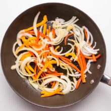 Sliced onions and bell peppers are being cooked in a skillet.