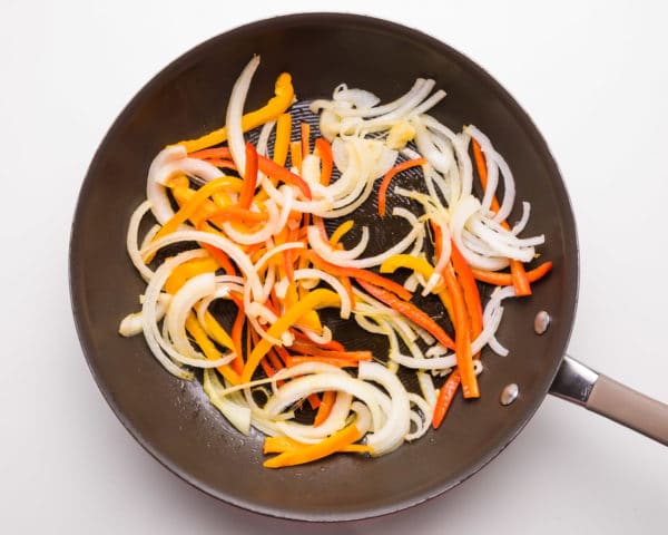 Sliced onions and bell peppers are being cooked in a skillet.