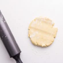 A rolling pin sits next to a pie dough disk on a white counter.