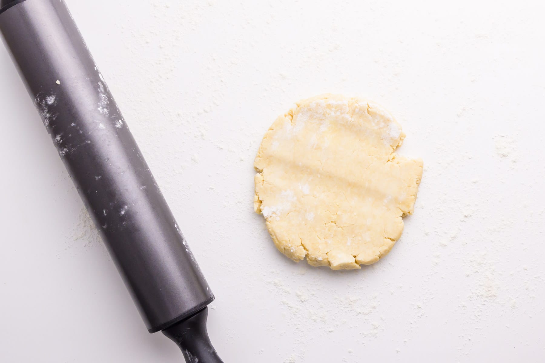A rolling pin sits next to a pie dough disk on a white counter.