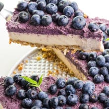 A slice of vegan raw cheesecake sits on a spatula and is hover over the rest of the dessert.
