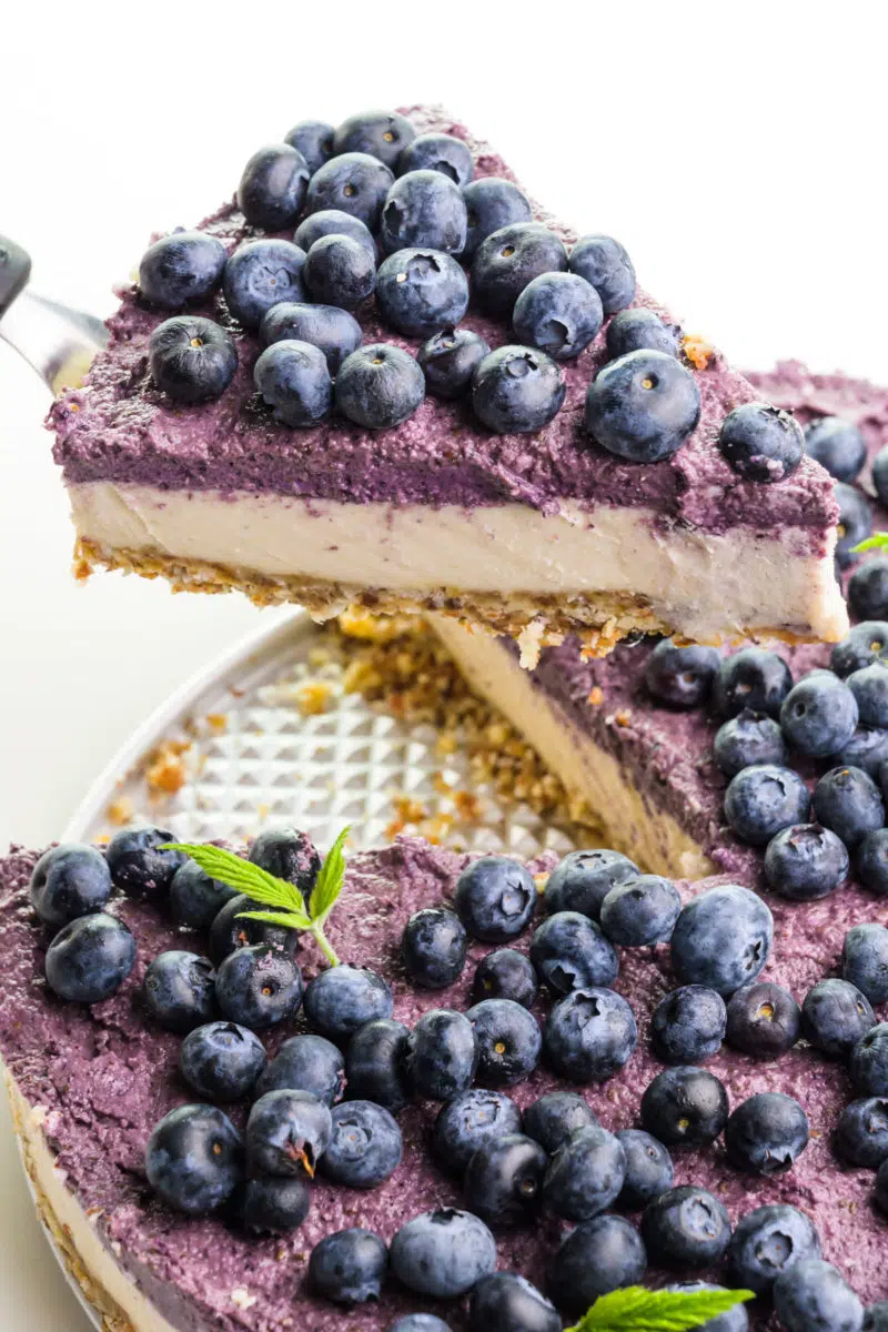 A slice of vegan raw cheesecake sits on a spatula and is hover over the rest of the dessert.
