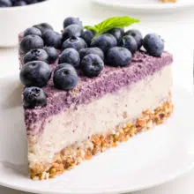 A slice of raw cheesecake has blueberries on top. It's sitting on a white plate.