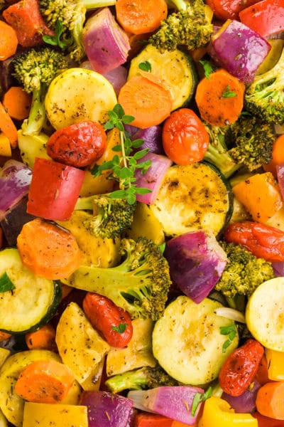 A closeup of vegetarian roasted vegetables with a sprig of fresh thyme in the middle.