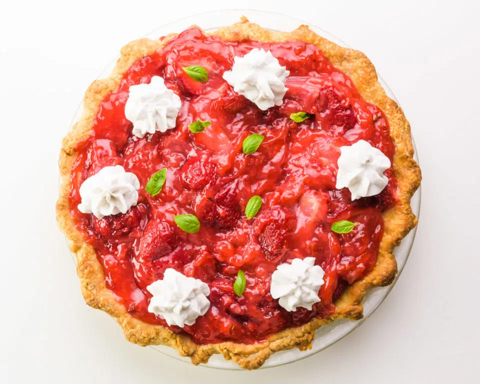 A strawberry pie has whipped cream and green herb leaves on top.