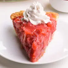A slice of vegan strawberry pie sits on a plate. It has coconut whipped cream on top.