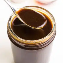 A closeup of vegan Worcestershire sauce in a spoon hovering over a mason jar full of more of the sauce.