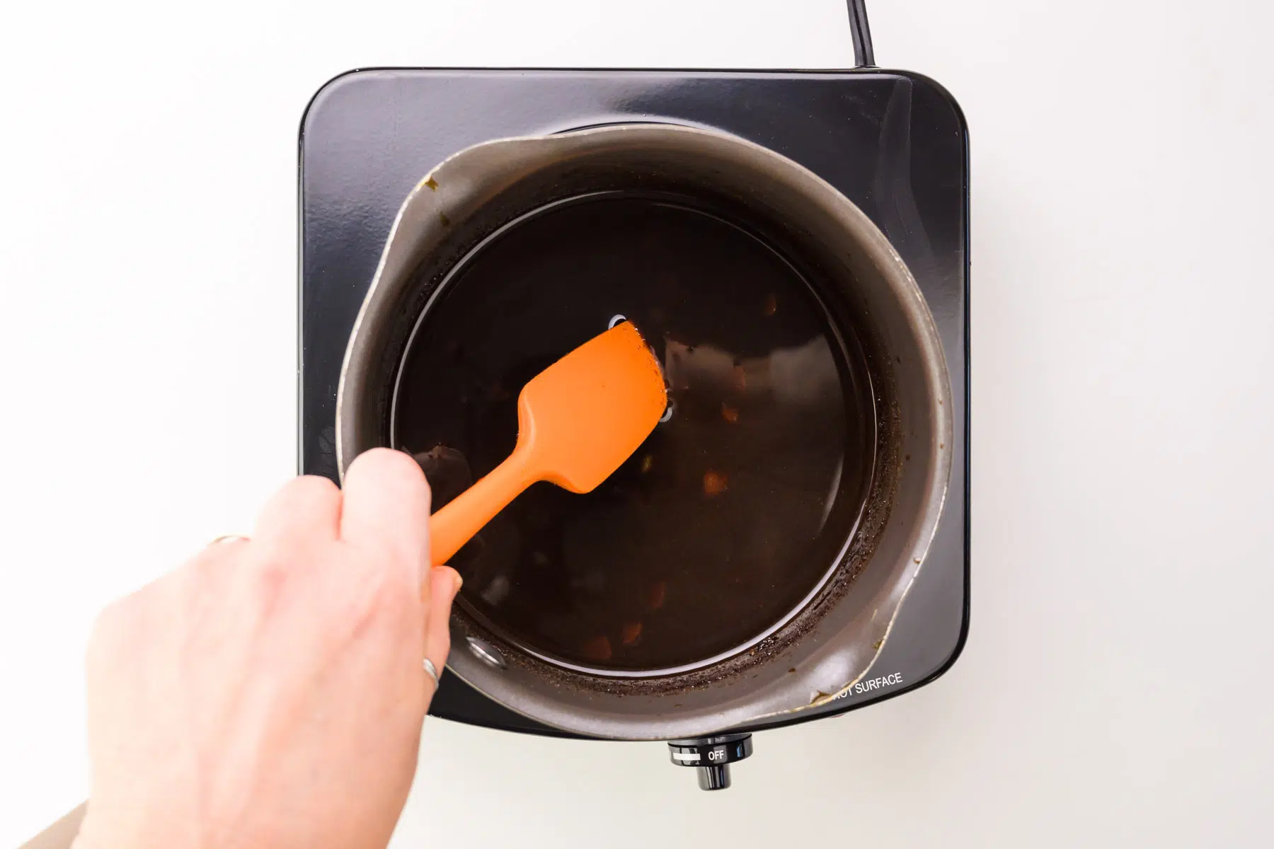 A dark sauce is simmering as a hand stirs it with a spatula.
