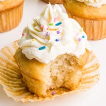 A vegan cake mix cupcake has a bite taken out. It sits in front of several other cupcakes.