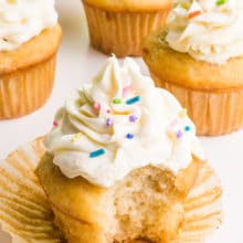 A veganized cake mix cupcake has a bite taken out. It sits in front of several other cupcakes.