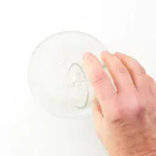 A hand holds a glass pouring warm water in with powdered egg replacer.