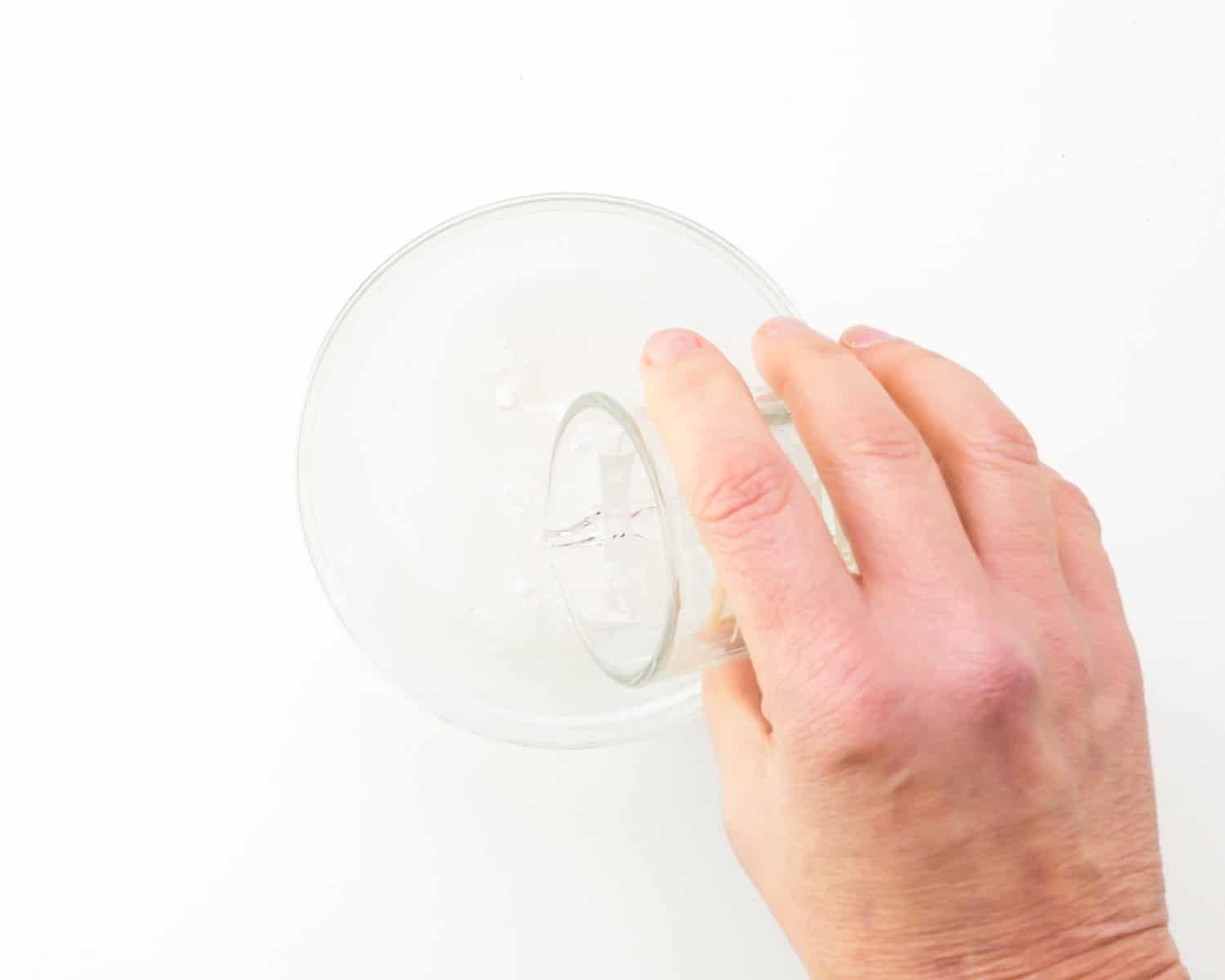 A hand holds a glass pouring warm water in with powdered egg replacer.