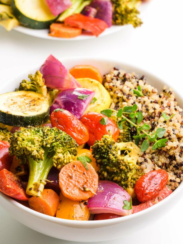 A bowl of vegan roasted veggies has quinoa on the side. There is a plate of vegetables in the background.