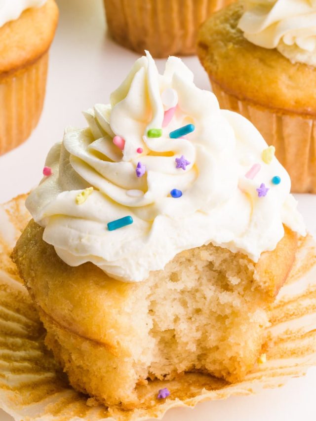 A veganized cake mix cupcake has a bite taken out. It sits in front of several other cupcakes.
