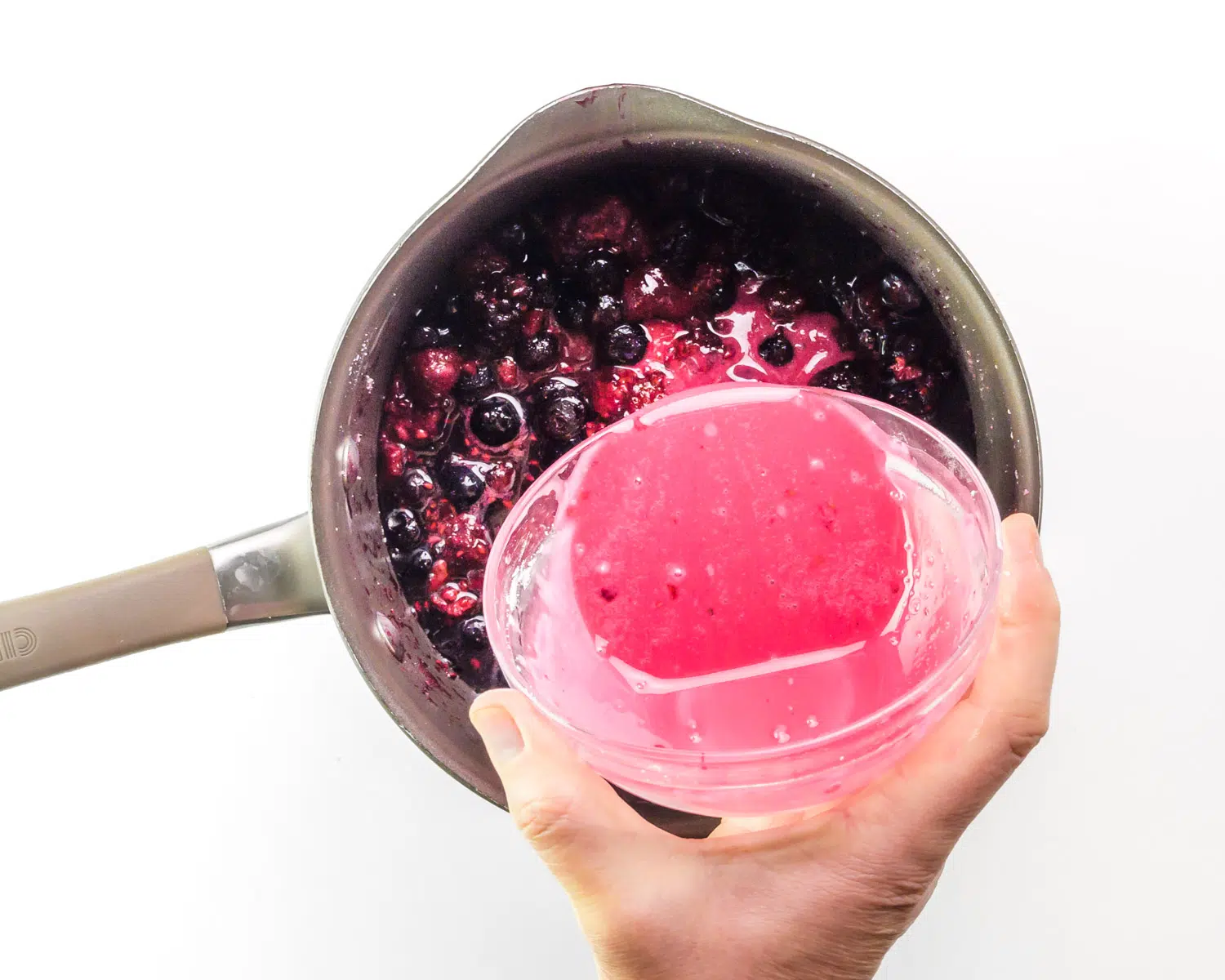 A berry slurry is being poured into a saucepan with more berries.