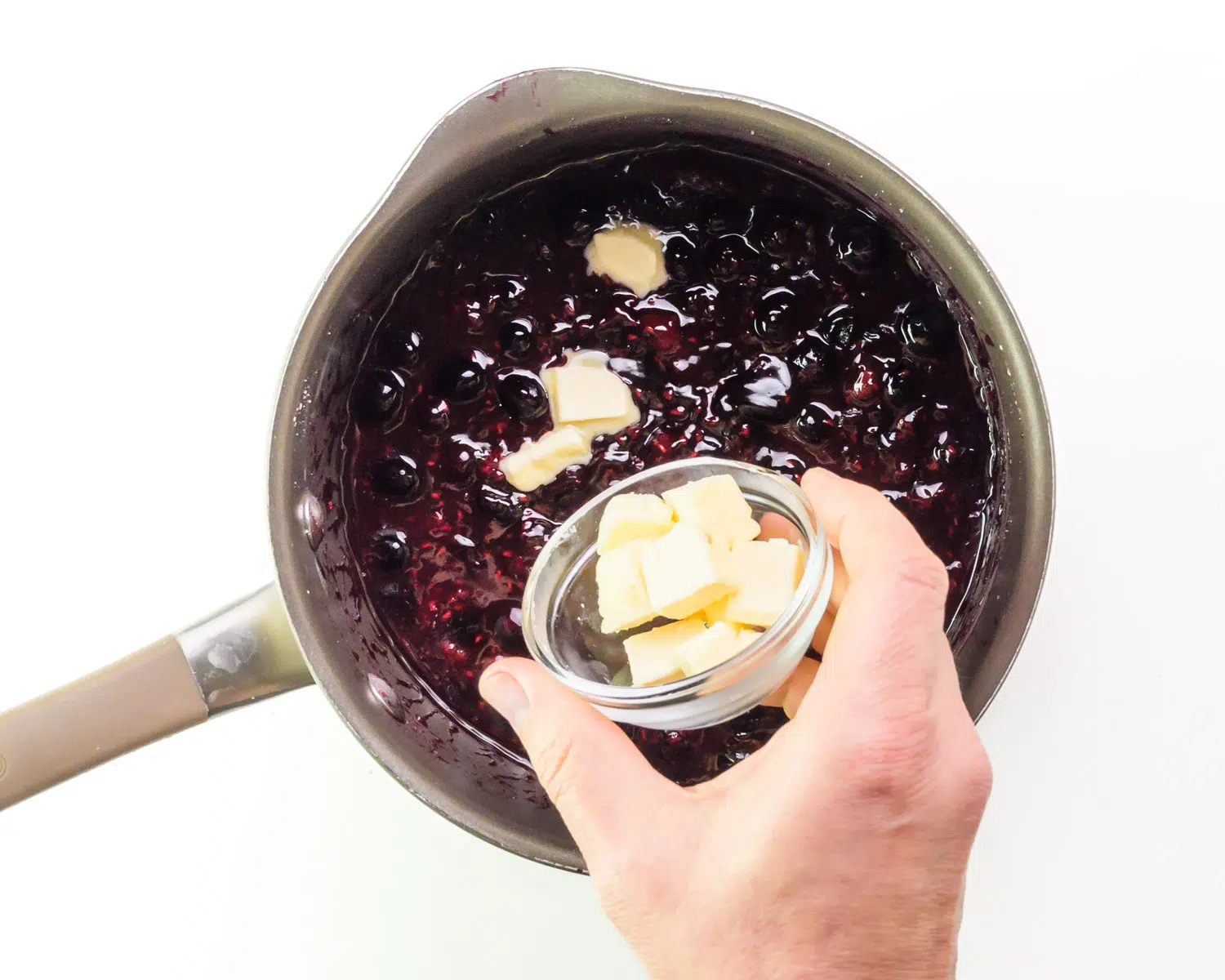 Vegan butter is being poured from a bowl into a saucepan with a berry sauce.