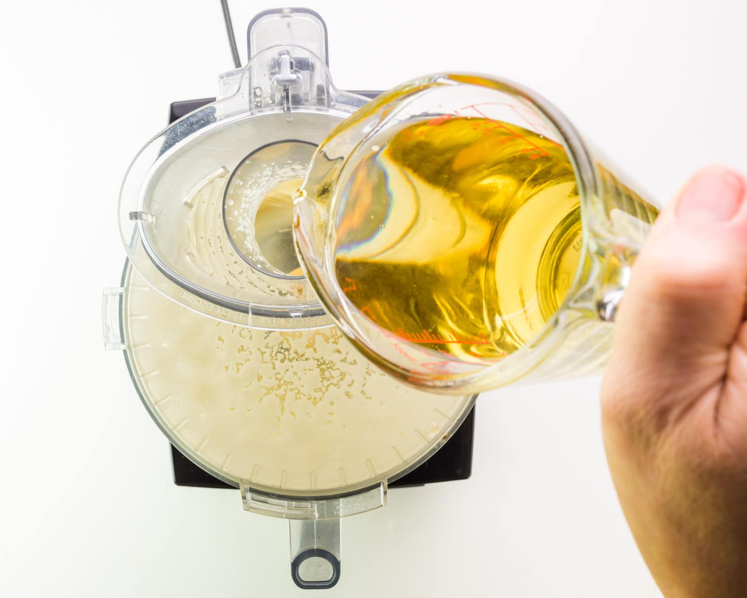 Vegetable oil is being poured into the top of a food processor as it's running.