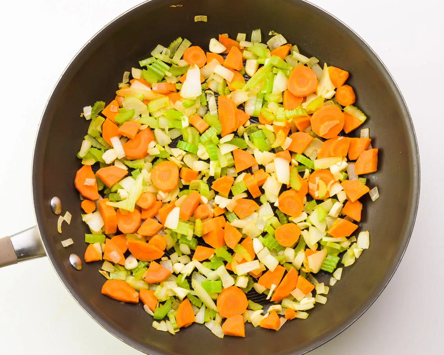 Carrots, onions, and celery are being cooked in a skillet.
