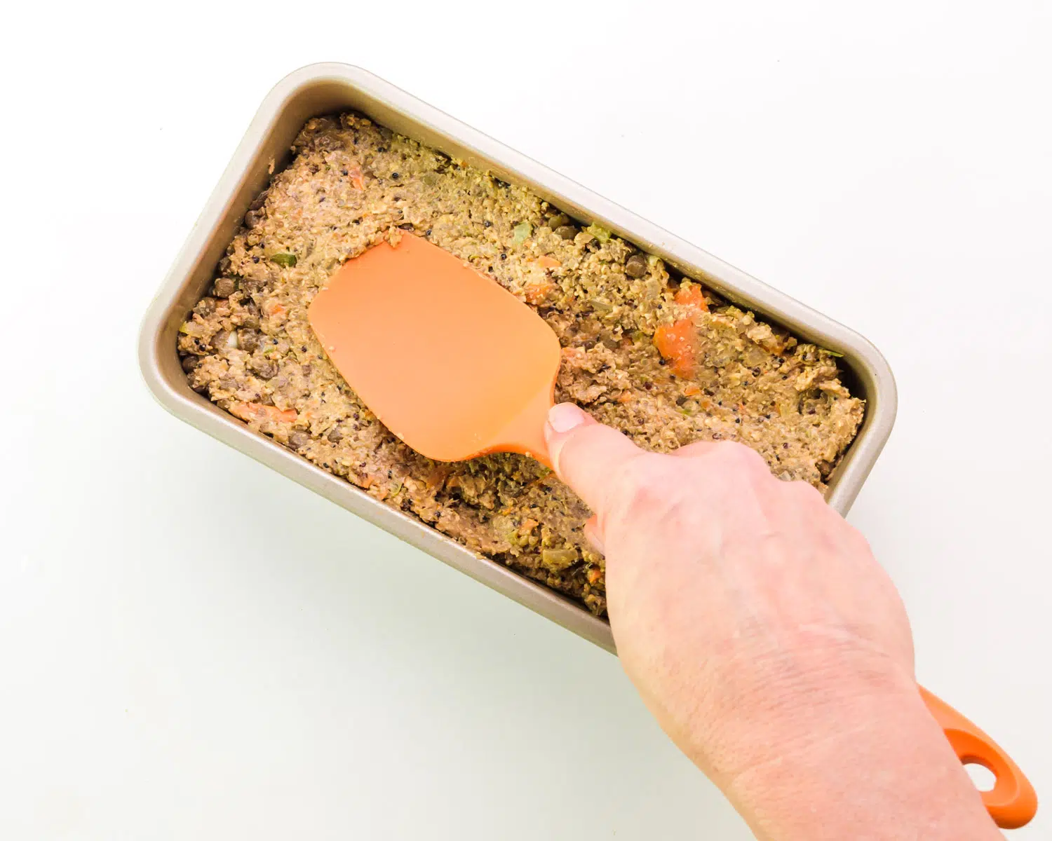 A hand holds a spatula, pressing a bean mixture into a loaf pan.