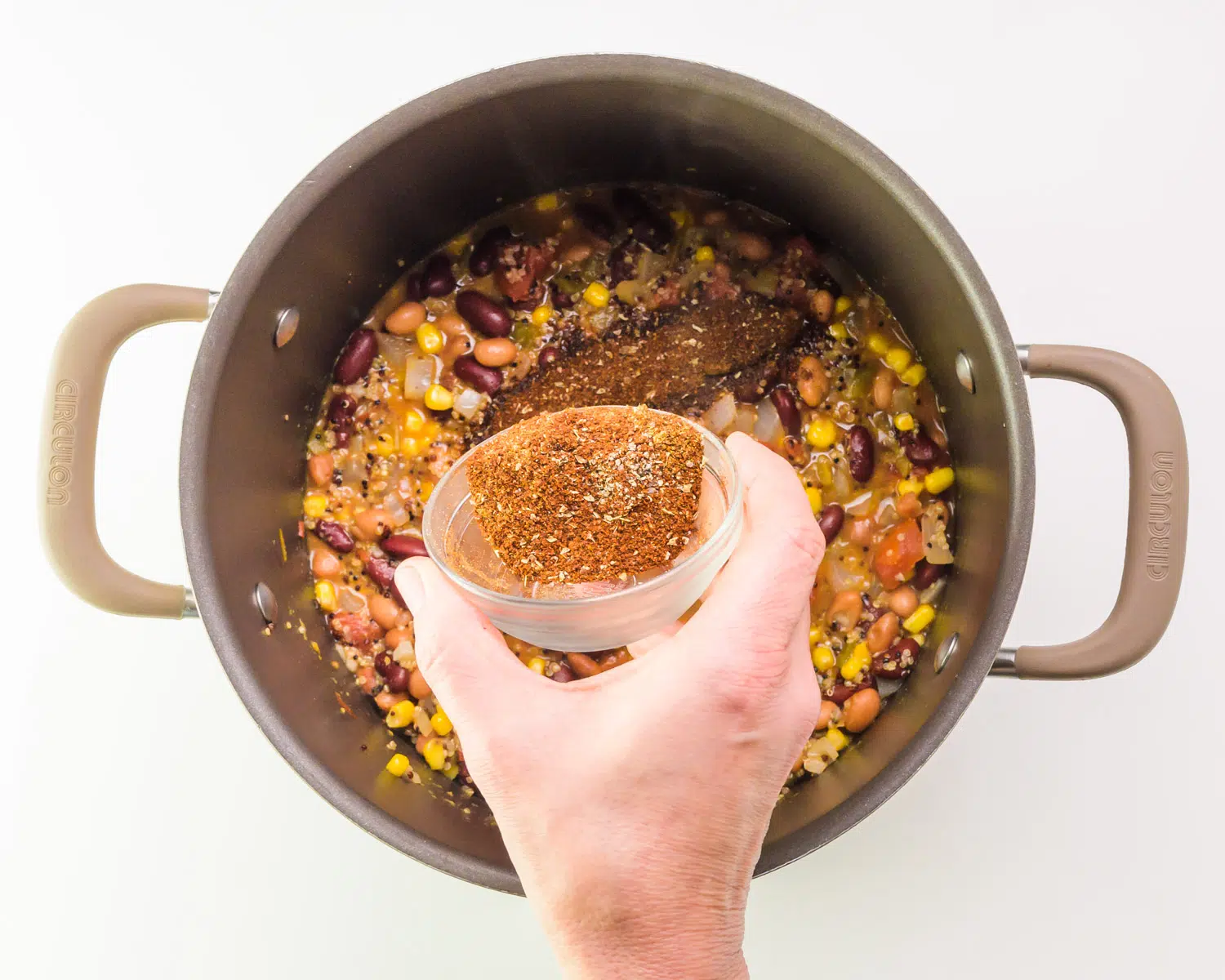 A hand holds a bowl of seasoning, pouring it into a pot of soup.