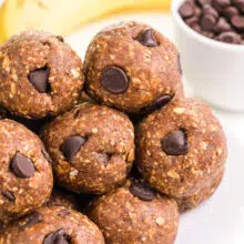 A plate of banana energy bites sits in front of a bowl of chocolate chips and a banana.