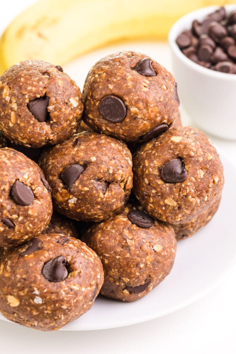 Looking down on a plate with banana energy balls sitting in front of a bowl of chocolate chips and a banana.
