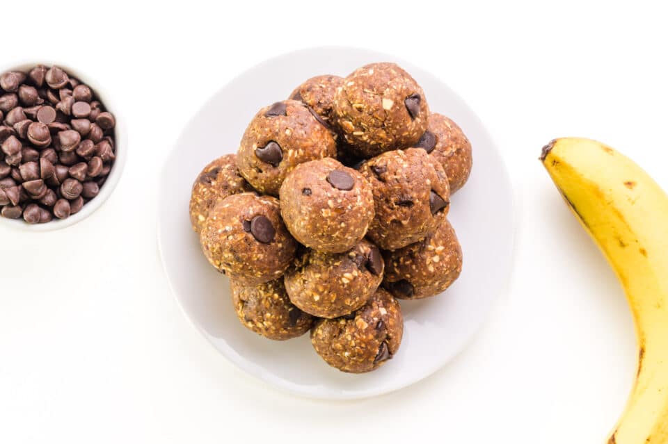 Look down at a plate of energy balls sitting next to a bowl of chocolate chips and a banana.