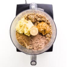 Ingredients are in a food processor, including peanut butter and mashed bananas.