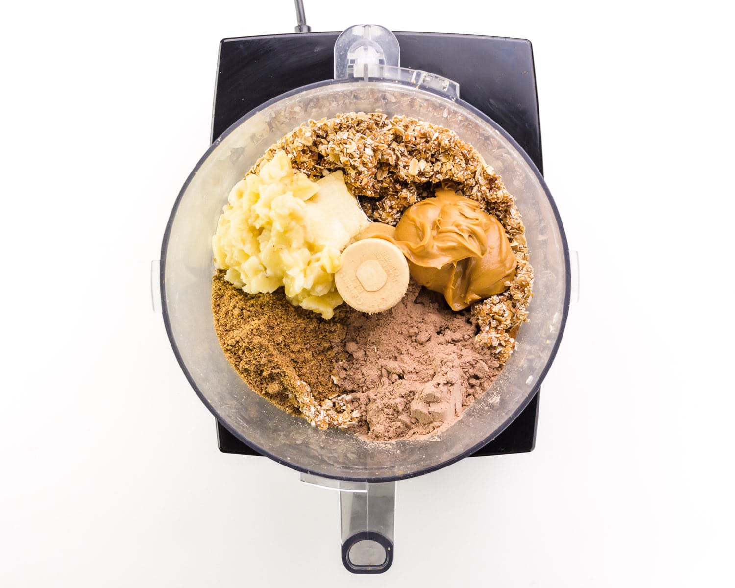 Ingredients are in a food processor, including peanut butter and mashed bananas.