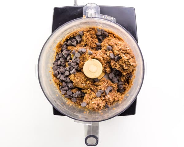 Chocolate chips have been added to energy ball ingredients in a food processor.