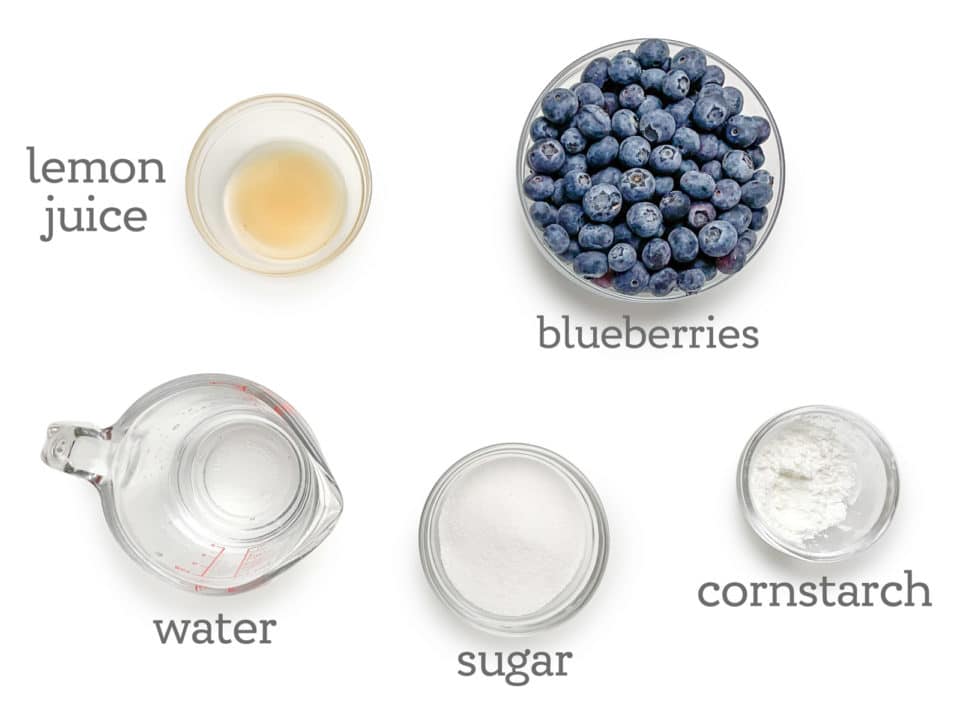 Ingredients are laid out on a table. The labels next to them read, blueberries, cornstarch, sugar, water, and lemon juice.
