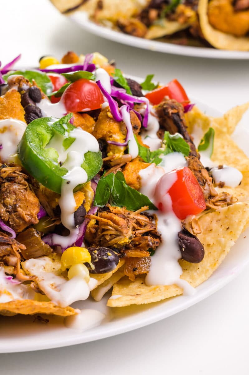 A plate of jackfruit nachos comes with chopped jalapeños, sour cream and more as toppings.  There is another plate in the background.